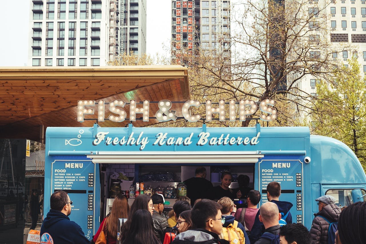 Crowd enjoying fish and chips at a lively food truck with urban buildings in the background.