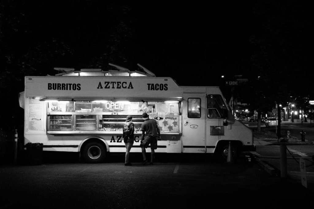 Black and white photo of people buying from a taco food truck at night.